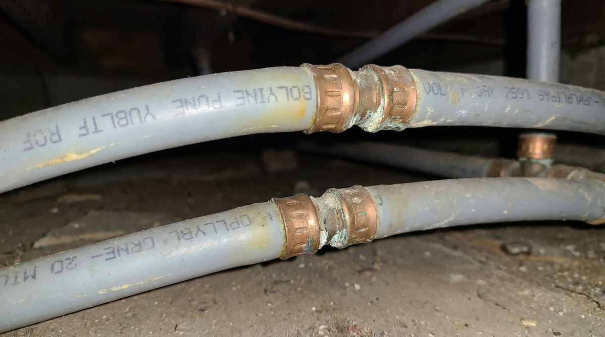 Gray polybutylene plumbing pipe with copper crimp rings from 1990s Gilbert Arizona home